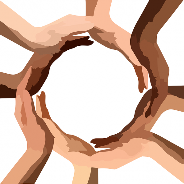 Hands of diverse races join together palm on top of hand to create a circle of the world.